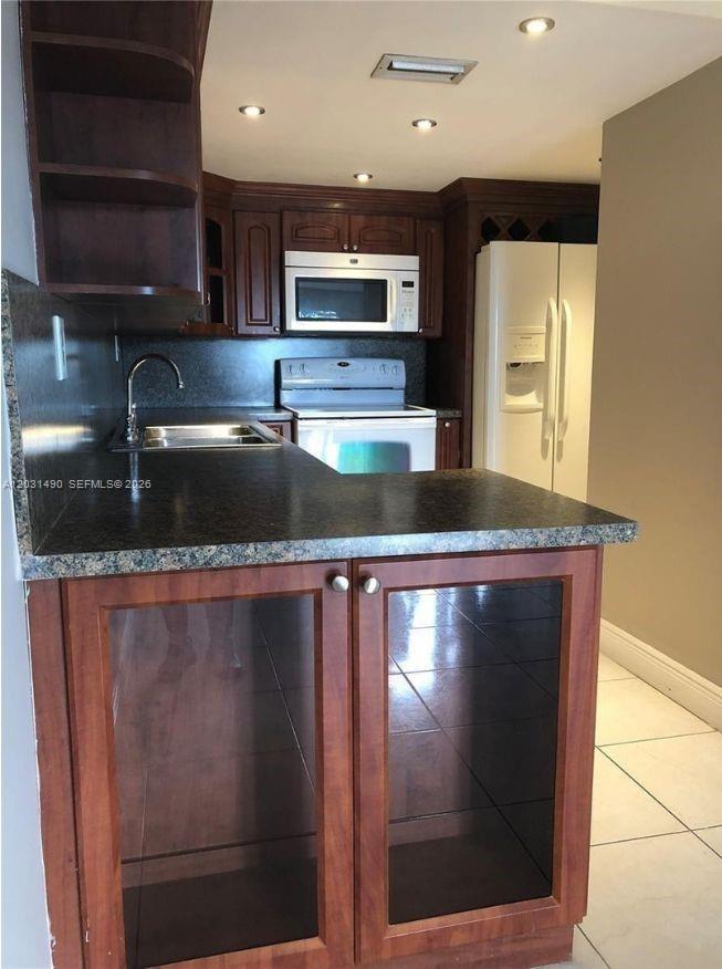 A kitchen features dark wood cabinets, a black countertop, a white stove, and glass-front cabinets — 14250 SW 62nd St # 325, Miami FL 33183, MIAMI, FL