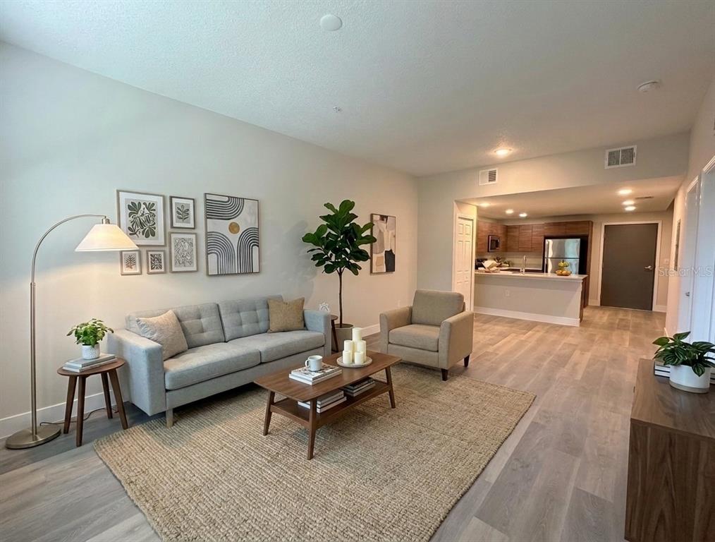A living room with a gray sofa, armchair, coffee table, and an open kitchen beyond — 4424 S TEXAS AVENUE UNIT 1-113, ORLANDO, FL