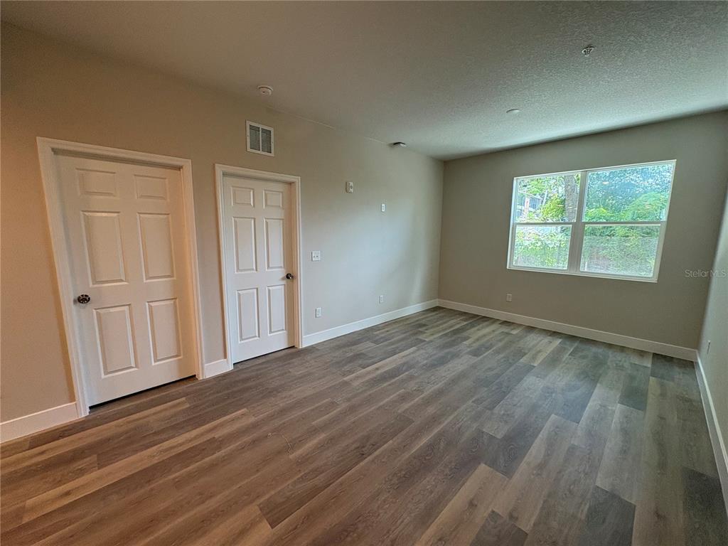 An empty room features wood-look flooring, two white doors, and a large window — 4424 S TEXAS AVENUE UNIT 1-113, ORLANDO, FL