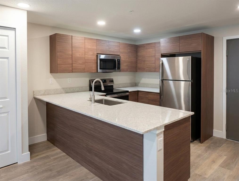 A modern kitchen features wood-grain cabinets, stainless steel appliances, and a light-colored quartz countertop island — 4424 S TEXAS AVENUE UNIT 1-113, ORLANDO, FL