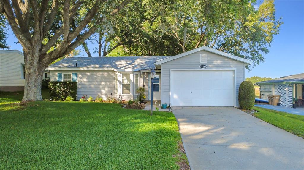 A single-story house with light gray siding, a front-facing garage, and a large shade tree — 25014 PINE HILL, LEESBURG, FL