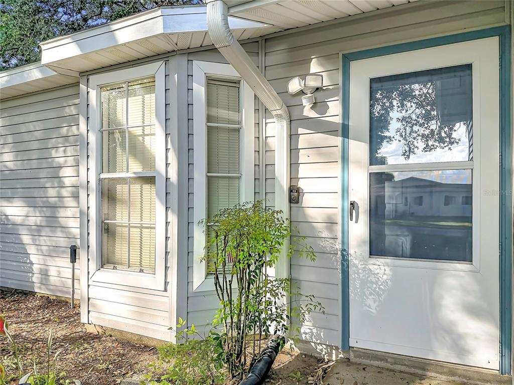 The exterior of a house features light-colored siding, a bay window, and a white door — 25014 PINE HILL, LEESBURG, FL