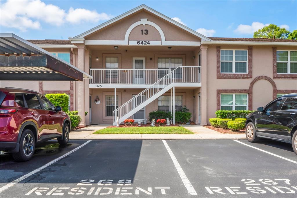 A two-story apartment building exterior with a staircase, parking spaces, and a covered carport — 6424 SPRING FLOWER DRIVE UNIT 24, NEW PORT RICHEY, FL