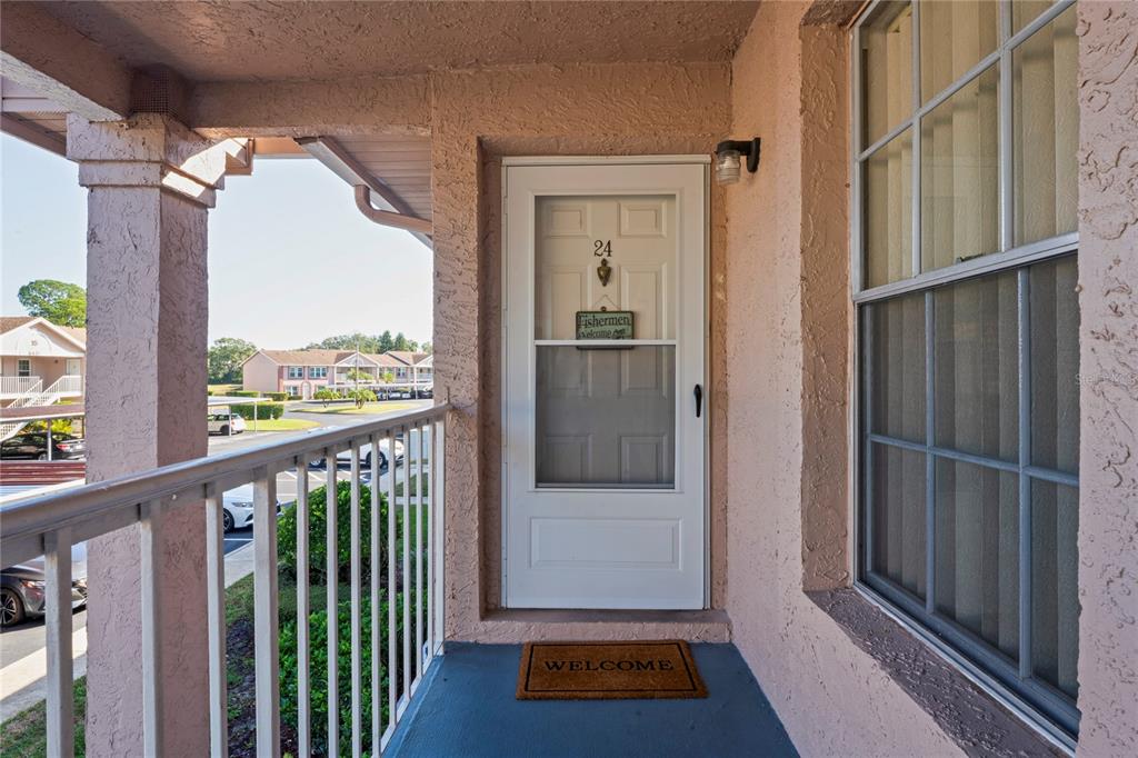 A covered entryway features a white storm door with a number 24 and a welcome mat — 6424 SPRING FLOWER DRIVE UNIT 24, NEW PORT RICHEY, FL