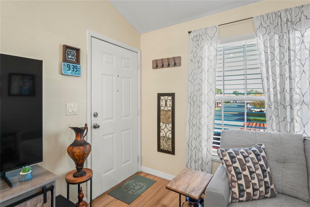A living room entrance features a white front door, a window with curtains, and furniture — 6424 SPRING FLOWER DRIVE UNIT 24, NEW PORT RICHEY, FL