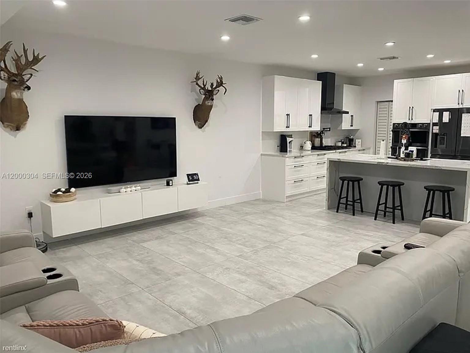 A modern open-concept living room and kitchen featuring white cabinetry, gray tile floors, and wall-mounted deer heads — 1935 SW 24th Ter, Miami FL 33145, MIAMI, FL