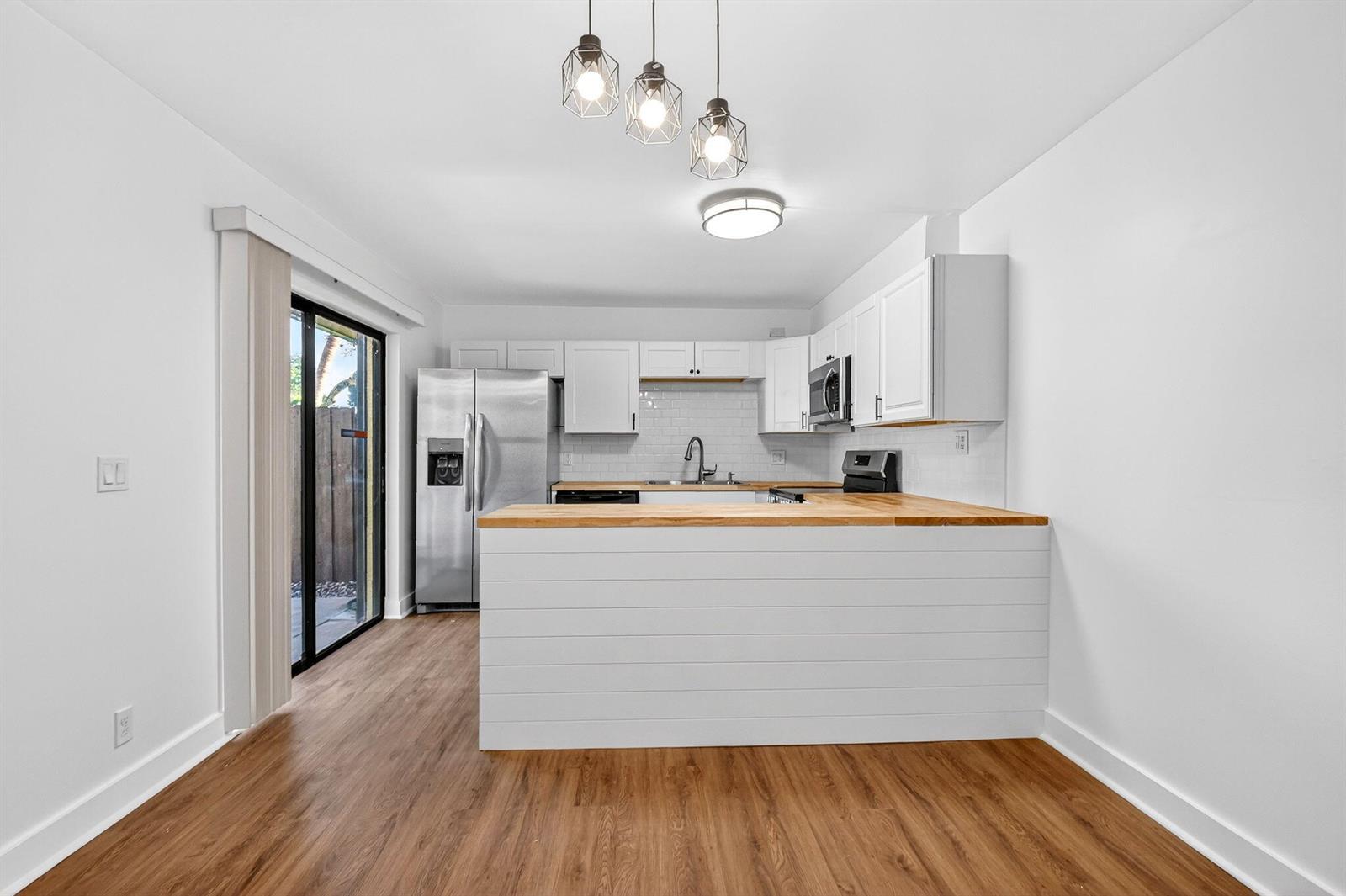 A kitchen features white cabinets, a wood countertop peninsula, and wood-look flooring — 198 Lake Arbor Drive, Palm Springs FL 33461, PALM SPRINGS, FL