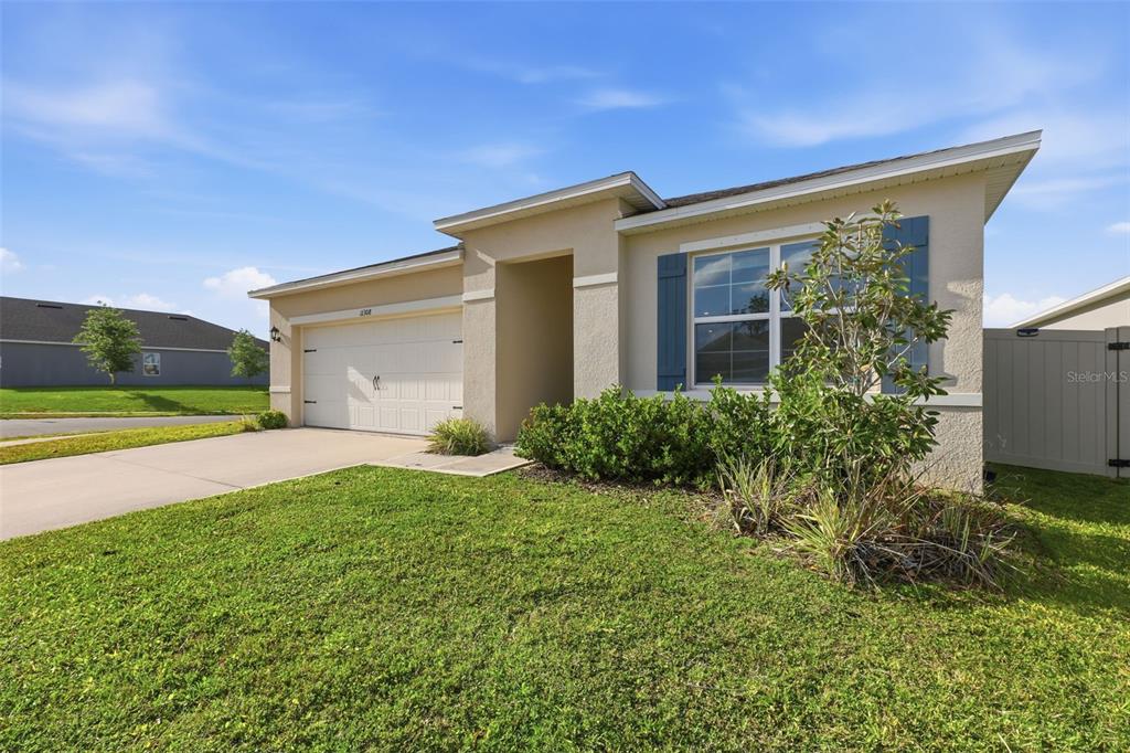 A single-story house with a beige stucco exterior, a two-car garage, and blue shutters — 11308 AMBER RIDGE DRIVE, ZELLWOOD, FL