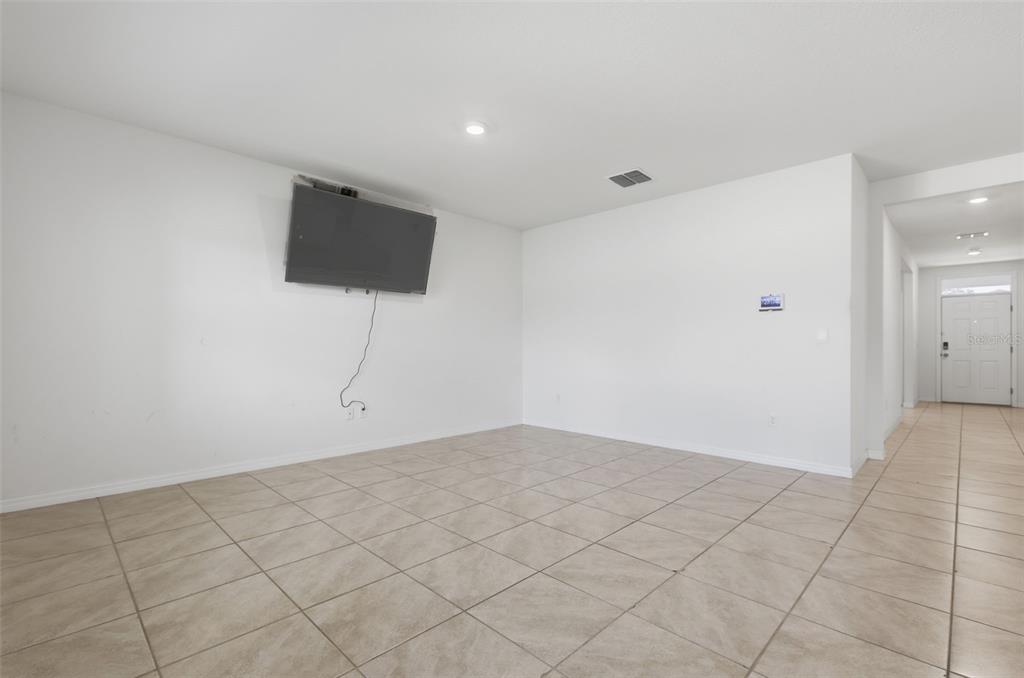 A living room features white walls, tile flooring, and a wall-mounted television — 11308 AMBER RIDGE DRIVE, ZELLWOOD, FL