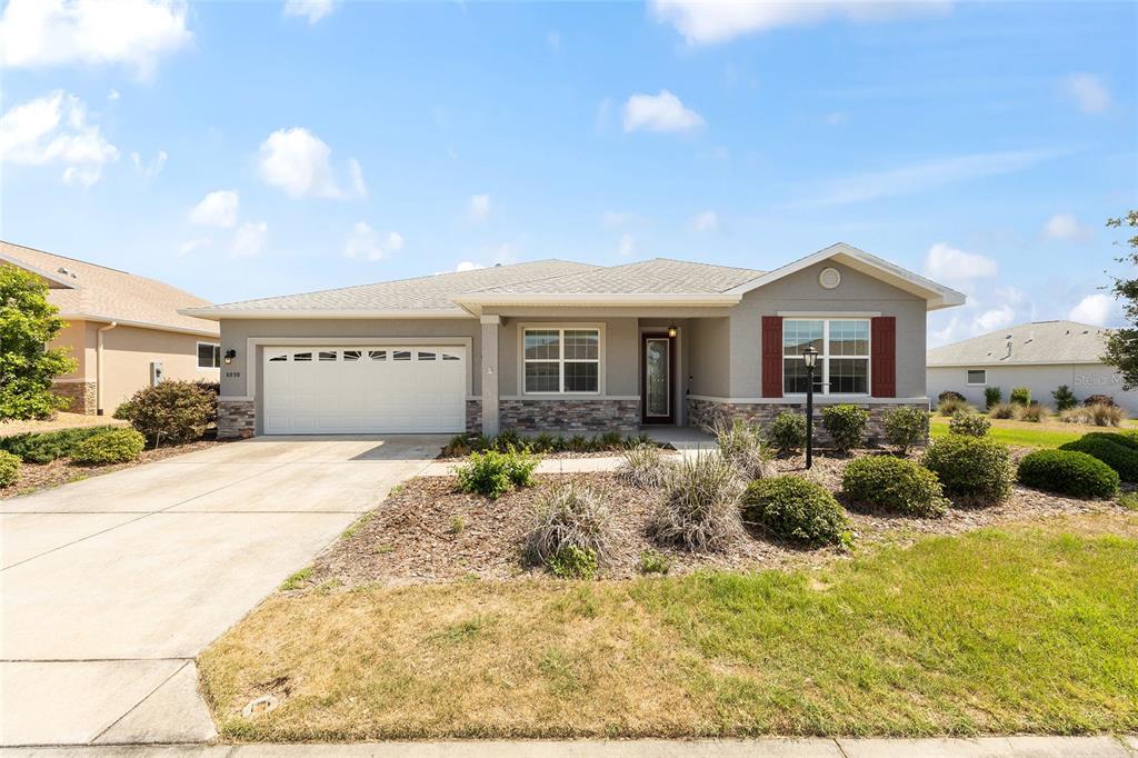 A single-story suburban house with a gray exterior, stone accents, and a two-car garage — 8898 SW 104TH CIRCLE, OCALA, FL