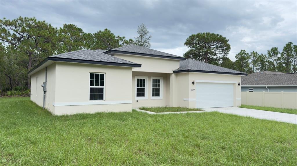 A single-story house with a beige stucco exterior, a white garage door, and a shingled roof — 6627 N HUNTINGTON TERRACE, CITRUS SPRINGS, FL