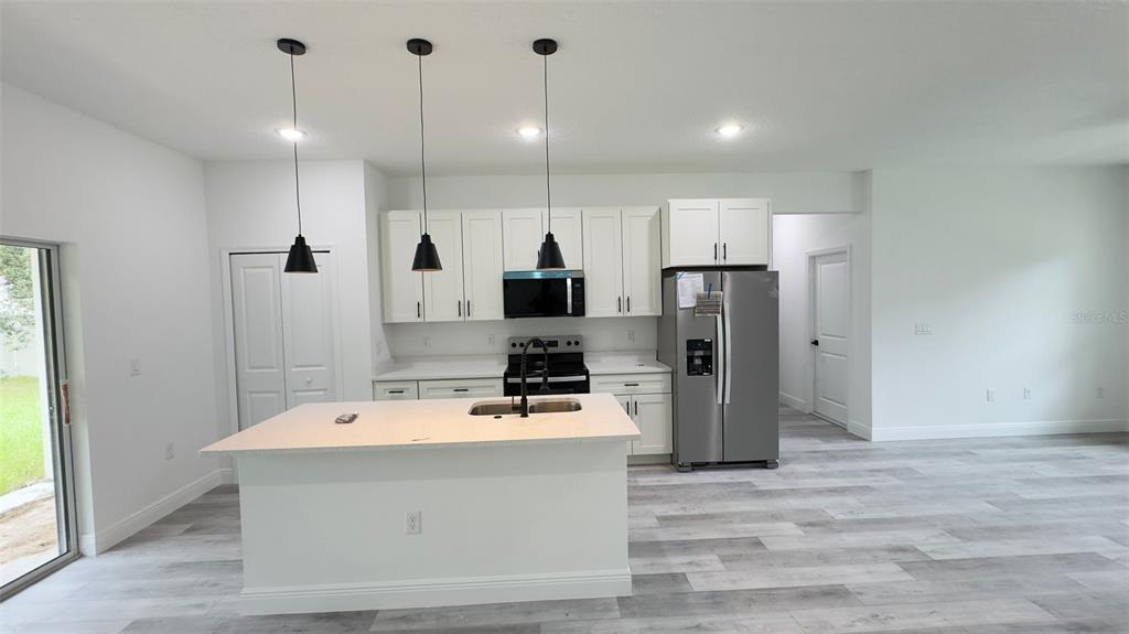 A modern kitchen features white cabinetry, a center island, stainless steel appliances, and gray flooring — 6627 N HUNTINGTON TERRACE, CITRUS SPRINGS, FL