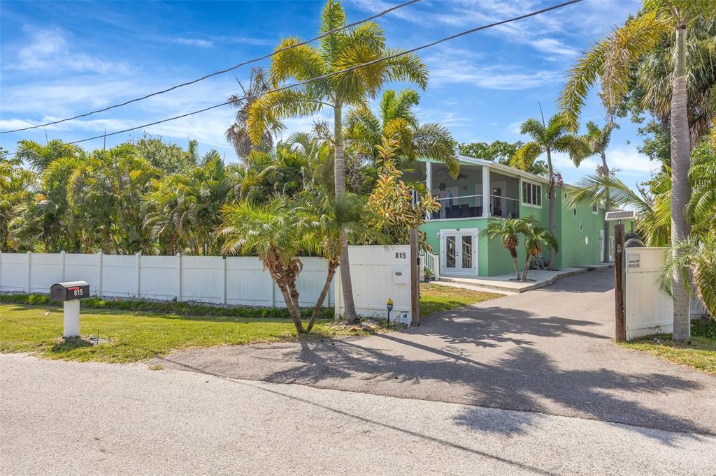 A two-story light green house with a gated driveway and palm trees in the yard — 815 2ND AVENUE NW, RUSKIN, FL