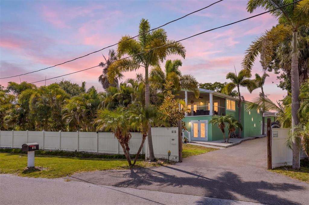 A green two-story house with a balcony and palm trees behind a white fence — 815 2ND AVENUE NW, RUSKIN, FL