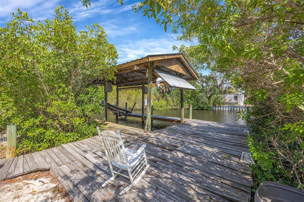 A wooden dock with a rocking chair and a covered boat lift sits by water — 815 2ND AVENUE NW, RUSKIN, FL