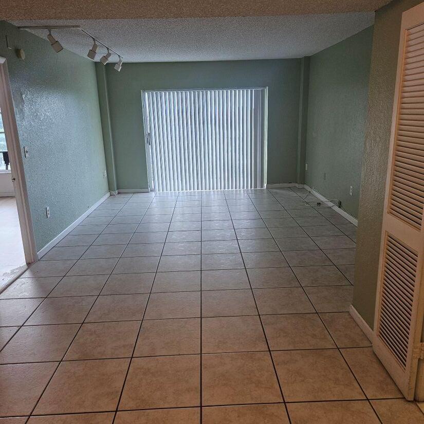 An empty room with light green walls, beige tile flooring, and a sliding glass door — 4174 Inverrary Drive # 603, Lauderhill FL 33319, LAUDERHILL, FL
