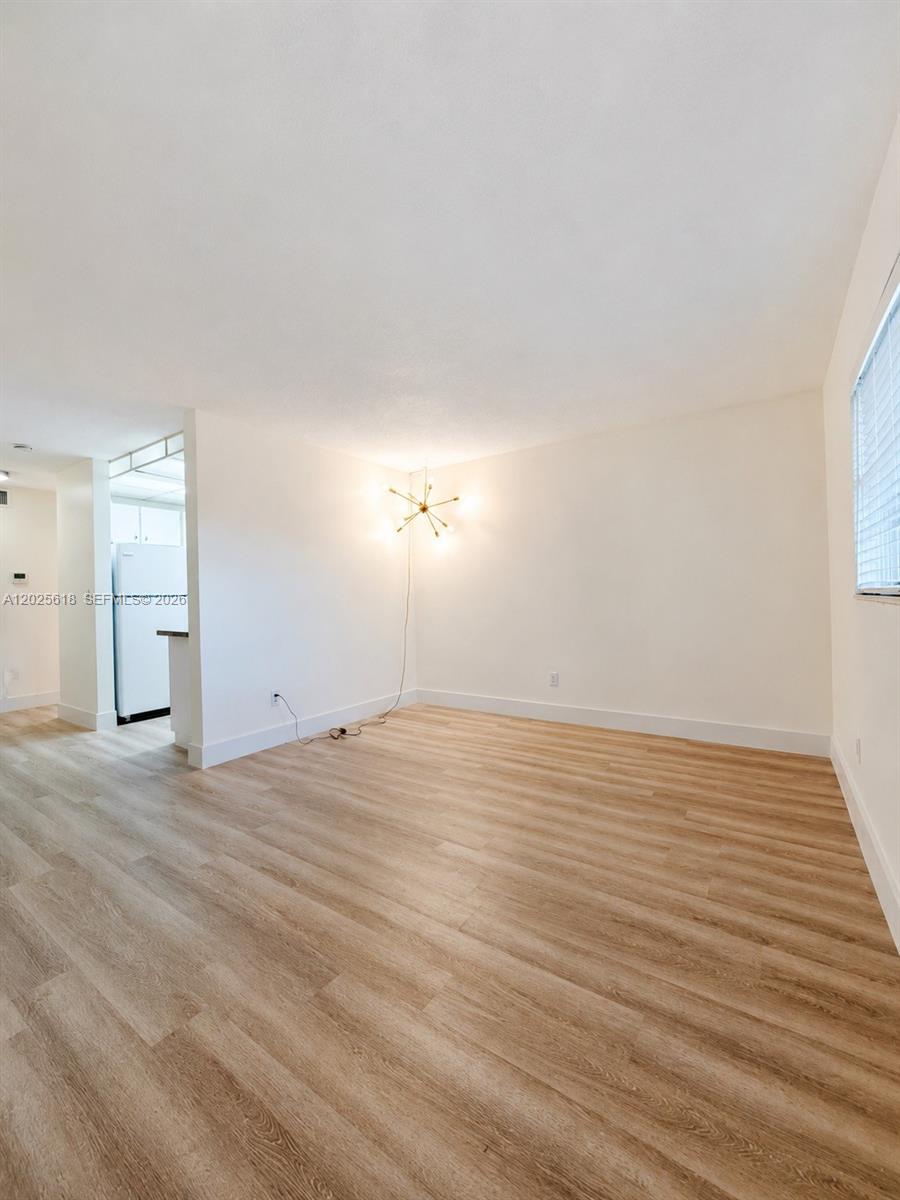 An empty room features light wood-look flooring, white walls, and a modern starburst wall light — 421 NE 1st St # 221, Hallandale Beach FL 33009, HALLANDALE BEACH, FL