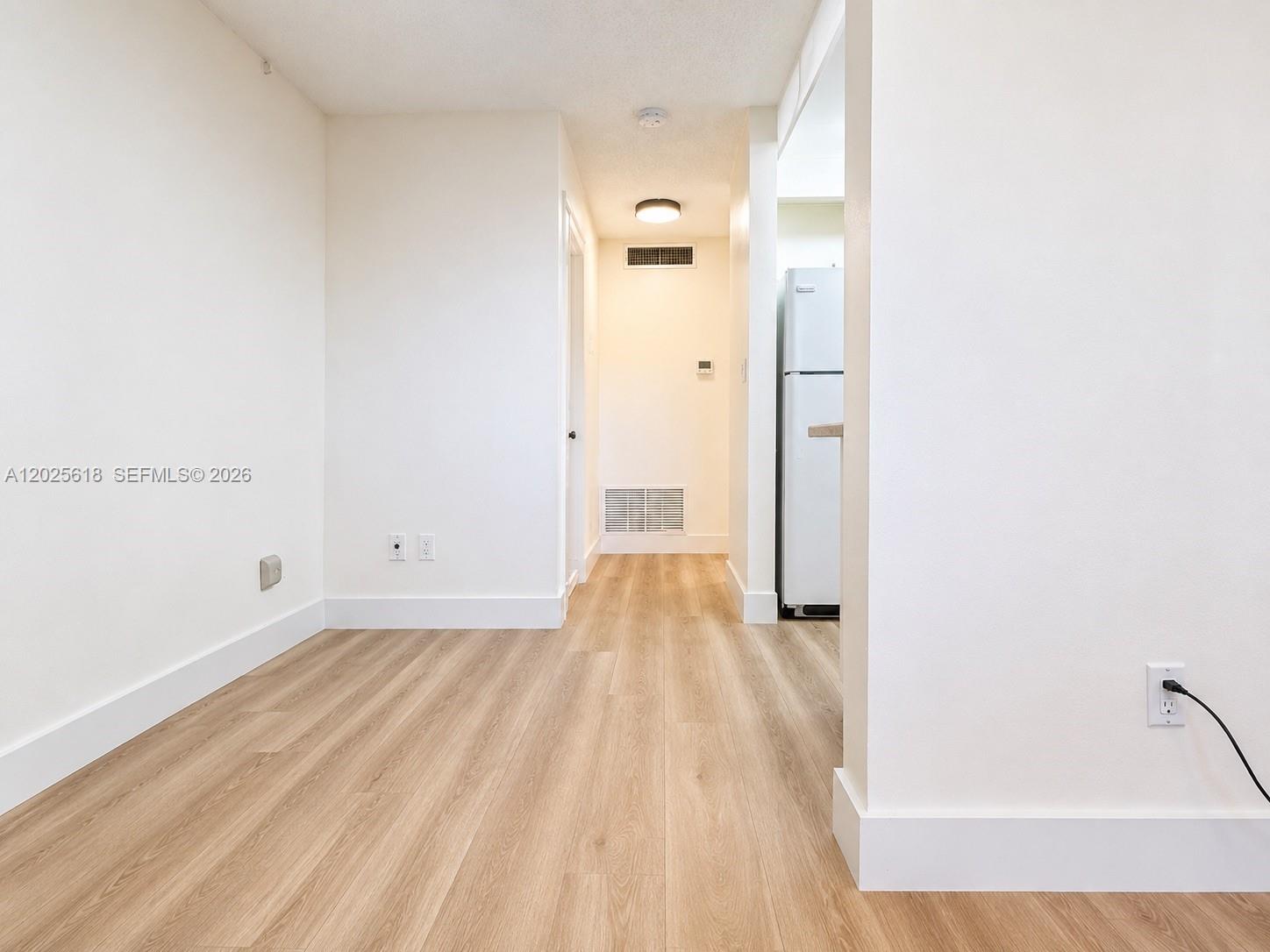 A bright room with light wood-look flooring leads to a hallway and a kitchen area — 421 NE 1st St # 221, Hallandale Beach FL 33009, HALLANDALE BEACH, FL