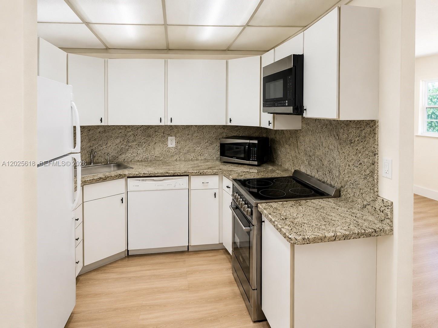 A kitchen features white cabinets, granite countertops, stainless steel appliances, and light wood flooring — 421 NE 1st St # 221, Hallandale Beach FL 33009, HALLANDALE BEACH, FL