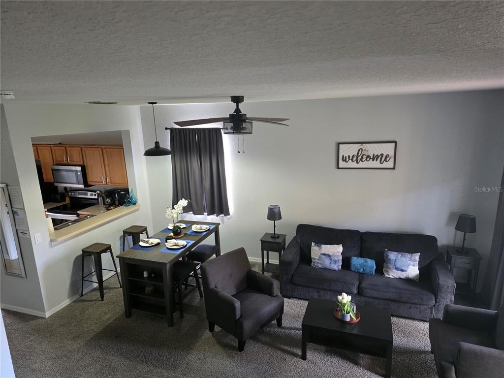 An open-concept living and dining area features a dark sofa, armchairs, and a kitchen pass-through — 746 TERRA LAGO STREET, DAVENPORT, FL