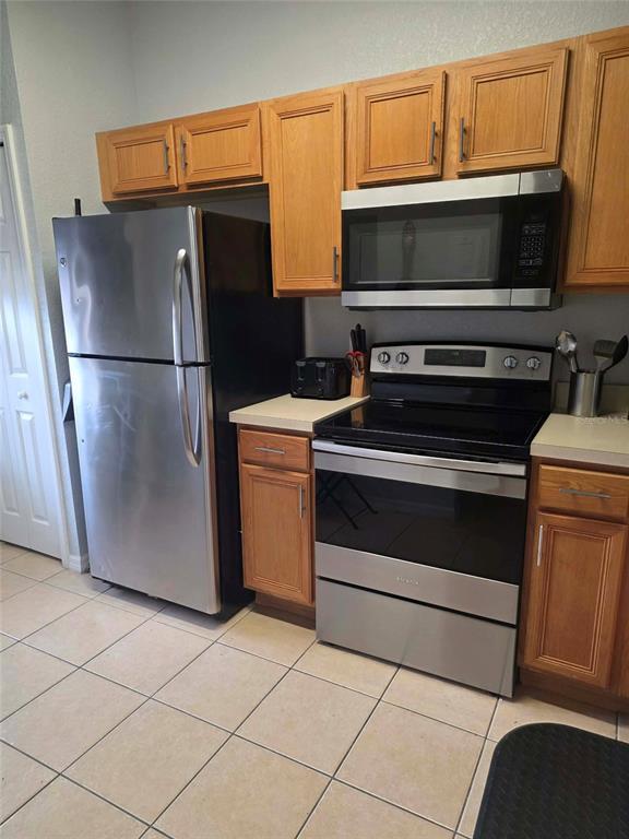 A kitchen features stainless steel appliances, wooden cabinets, and light-colored tile flooring — 746 TERRA LAGO STREET, DAVENPORT, FL