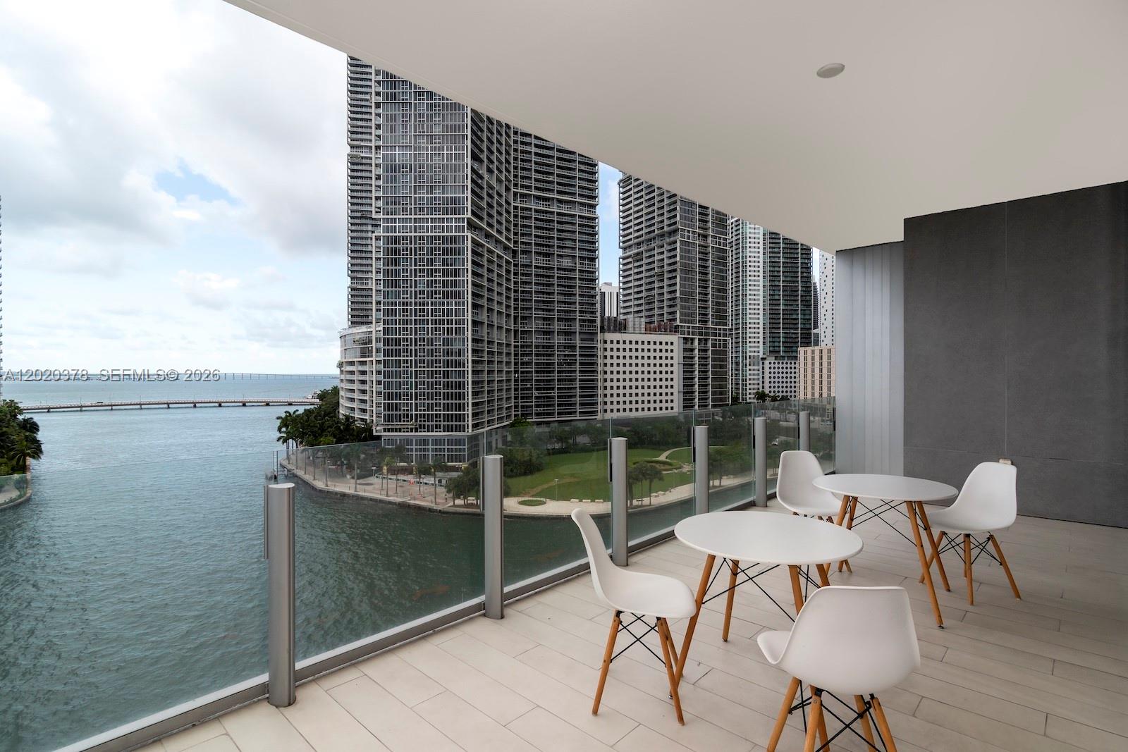 A balcony with white tables and chairs overlooks a bay and city skyline — 300 Biscayne Boulevard Way # 802E, Miami FL 33131, MIAMI, FL