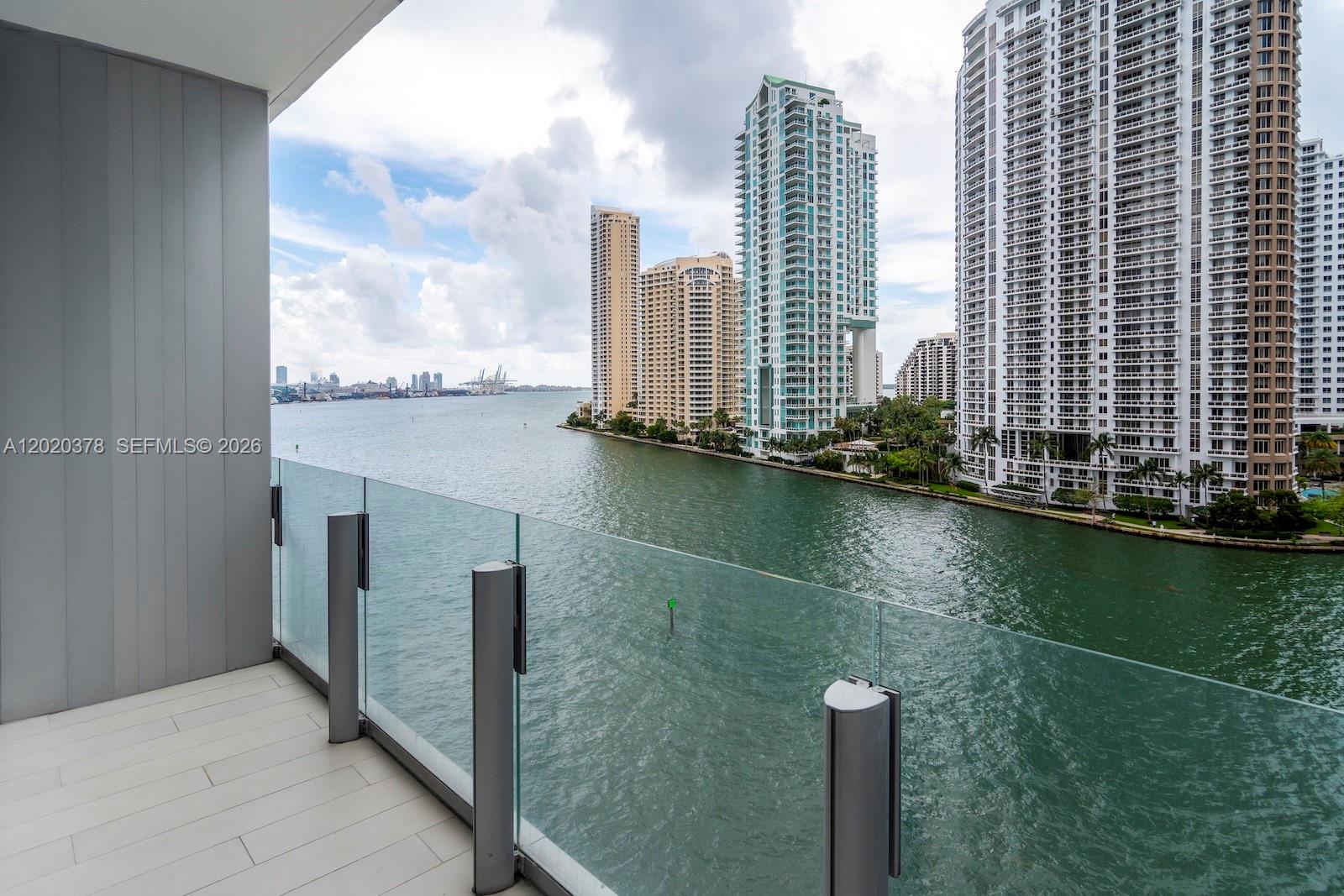 A balcony with a glass railing overlooks a waterway and high-rise buildings — 300 Biscayne Boulevard Way # 802E, Miami FL 33131, MIAMI, FL