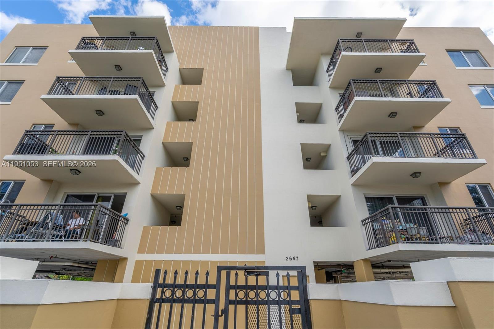 A low-angle view of a multi-story apartment building exterior with balconies and a metal gate — 2647 NW 25th Ave # 507, Miami FL 33142, MIAMI, FL