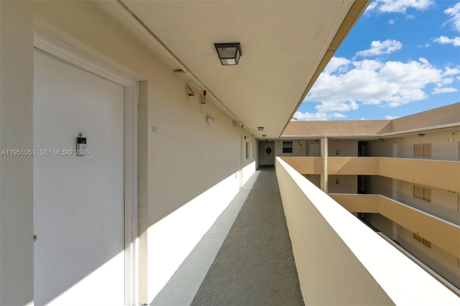 An outdoor apartment building walkway features a white door, concrete flooring, and a balcony railing — 2647 NW 25th Ave # 507, Miami FL 33142, MIAMI, FL