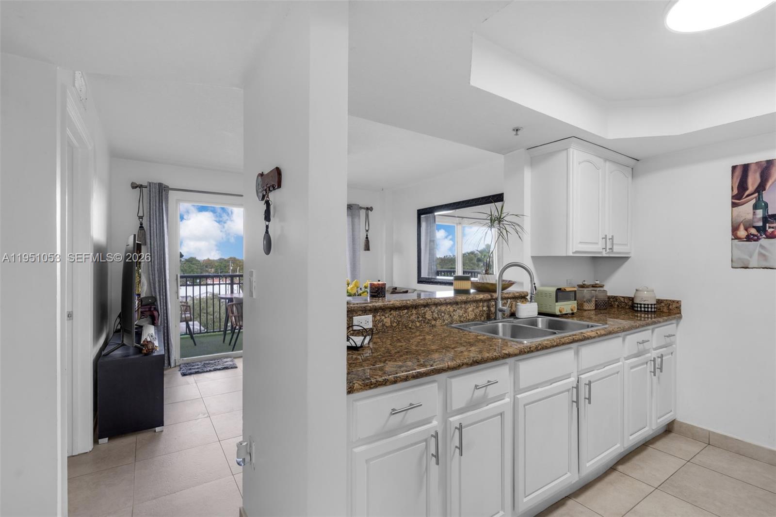 A kitchen with white cabinets and granite countertops overlooks a living area and balcony — 2647 NW 25th Ave # 507, Miami FL 33142, MIAMI, FL