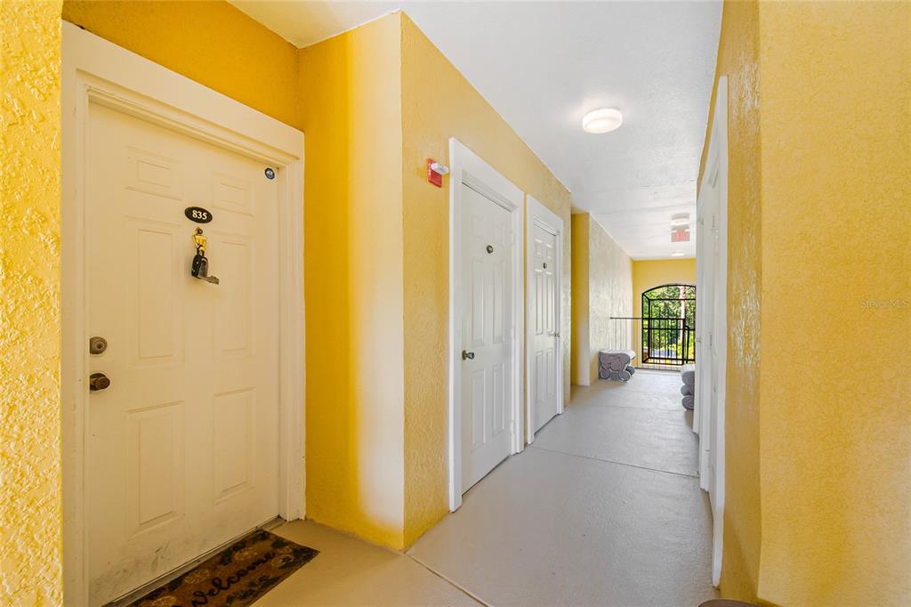 An outdoor apartment hallway features yellow walls, white doors, and a concrete floor — 3611 CONROY ROAD UNIT 835, ORLANDO, FL