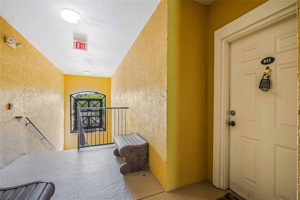 A yellow-walled apartment hallway features a white door labeled 835, a bench, and stairs — 3611 CONROY ROAD UNIT 835, ORLANDO, FL