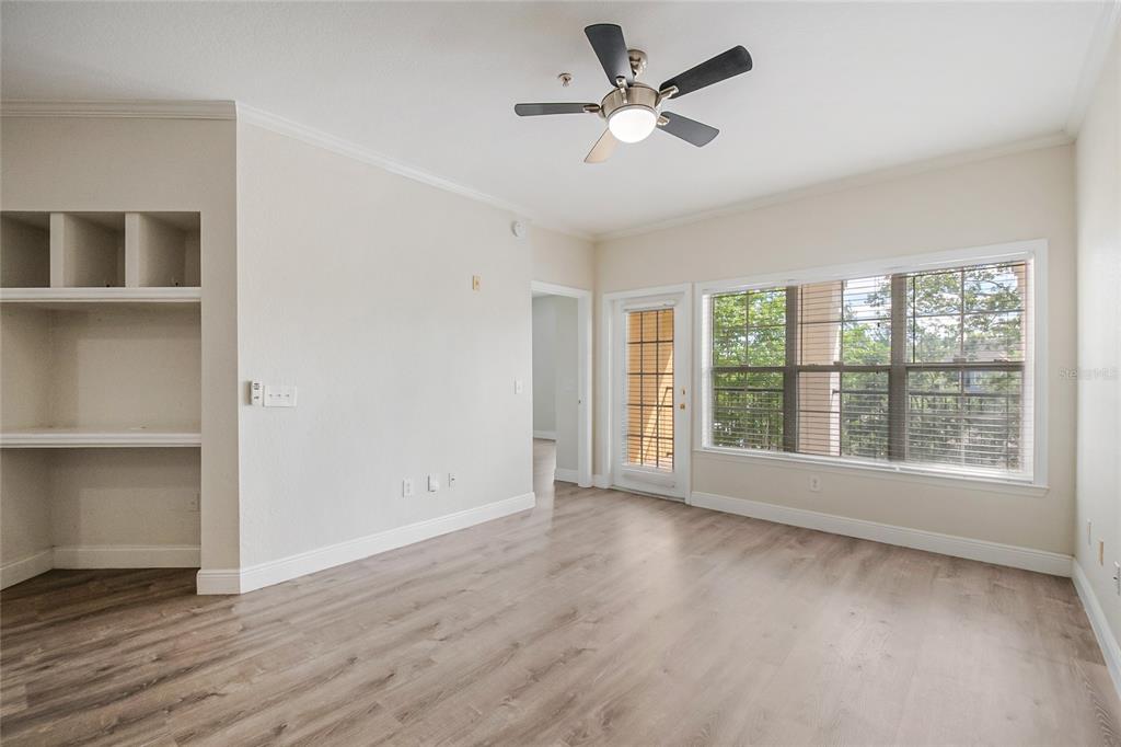 An empty room features light wood-look flooring, a ceiling fan, built-in shelving, and a balcony door — 3611 CONROY ROAD UNIT 835, ORLANDO, FL