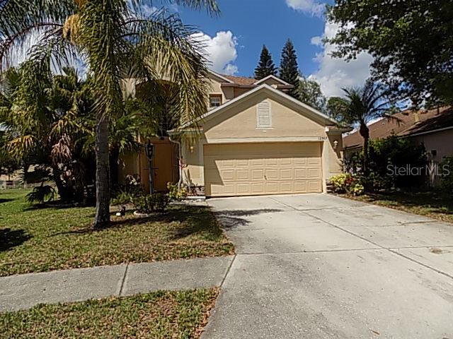 A two-story tan house features a two-car garage and a palm tree in the front — 12507 ROCKROSE GLEN, LAKEWOOD RANCH, FL