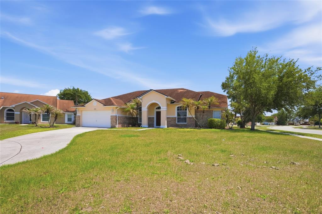 A single-story suburban house with a tan stucco exterior, brick accents, and a two-car garage — 2415 TIMOTHY LANE, KISSIMMEE, FL