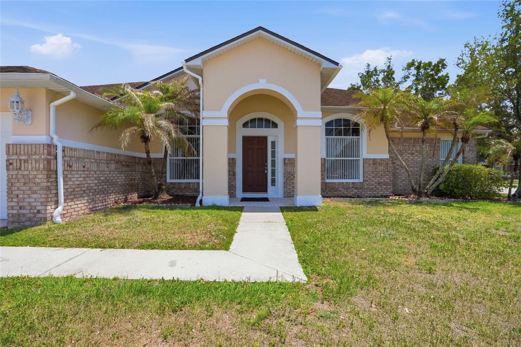 A single-story house with a tan stucco exterior, brick accents, and a central arched entryway — 2415 TIMOTHY LANE, KISSIMMEE, FL