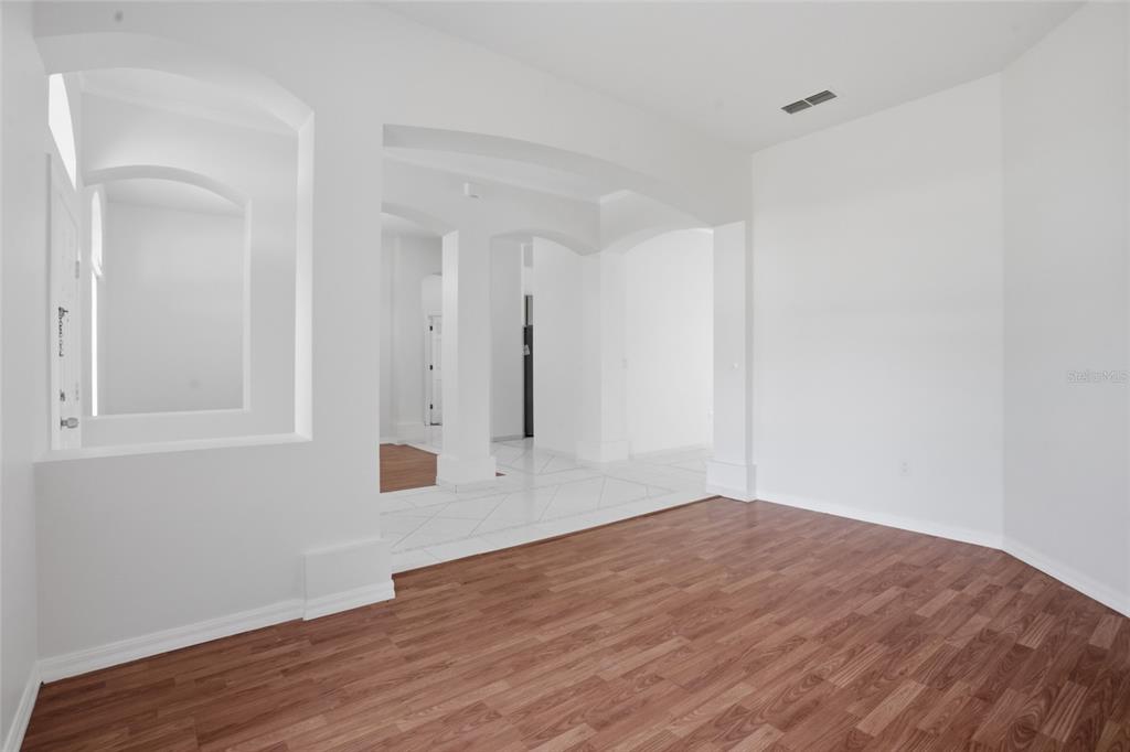 An empty room features wood-look flooring, white walls, arched architectural details, and tiled transition areas — 2415 TIMOTHY LANE, KISSIMMEE, FL