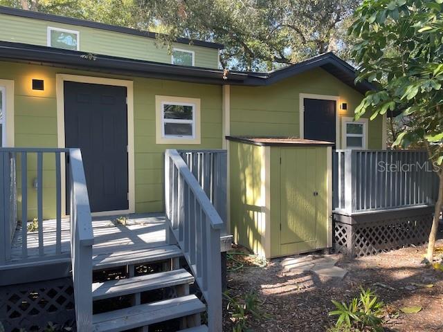 A light green house exterior features dark doors, a wooden deck, and a small storage shed — 1157 HIGHLAND COURT N, ST PETERSBURG, FL