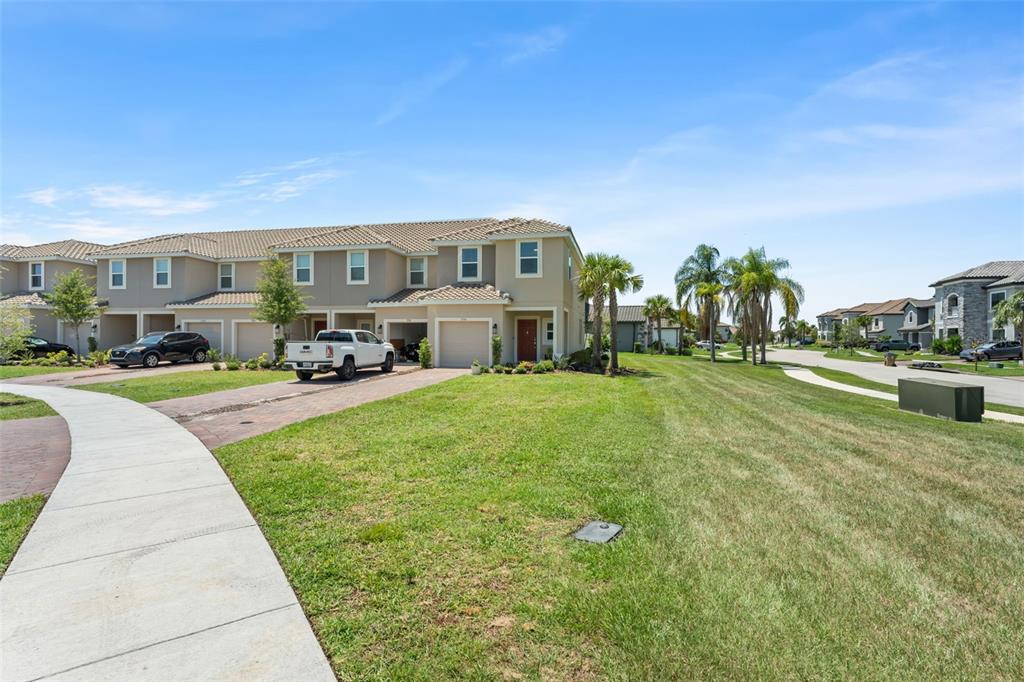 A row of two-story townhouses with attached garages and a paved driveway under a blue sky — 3556 LANDING NET DRIVE, KISSIMMEE, FL