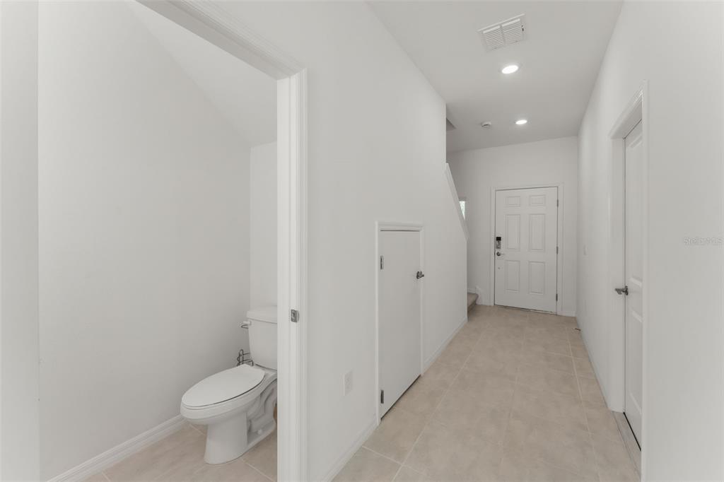 A hallway with tile flooring leads to a front door, featuring a small under-stair closet — 3556 LANDING NET DRIVE, KISSIMMEE, FL