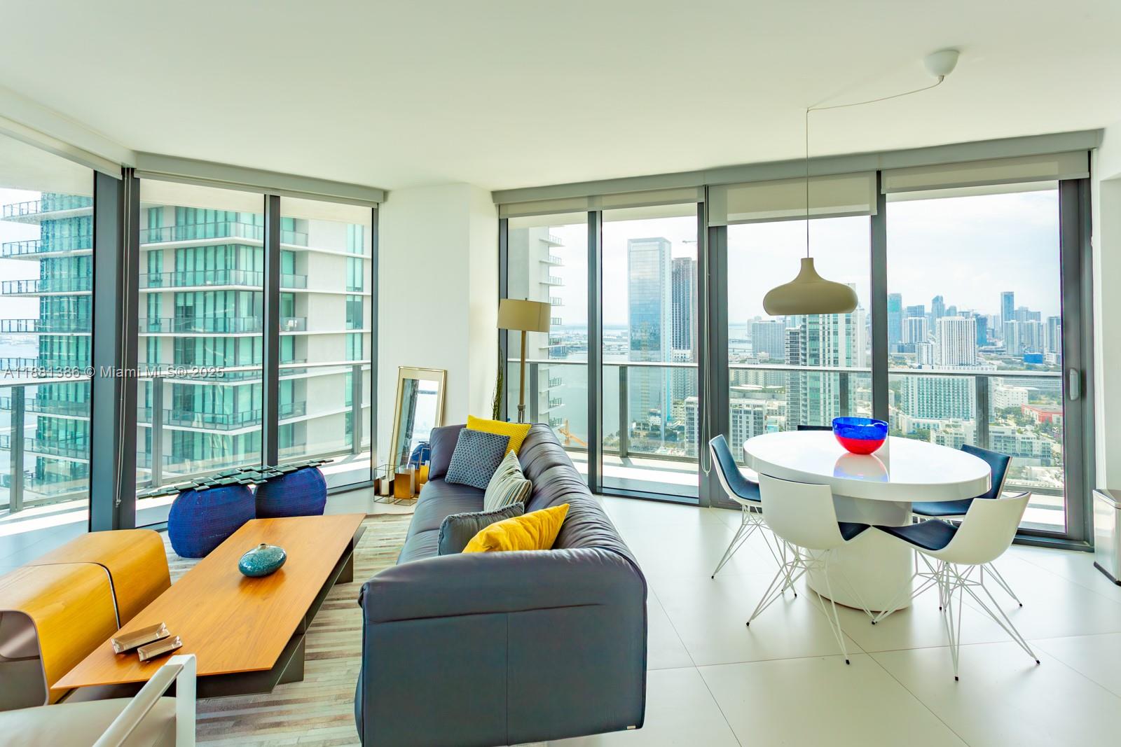 A modern living and dining area features floor-to-ceiling windows with expansive city and water views — 501 NE 31st St # 3906, Miami FL 33137, MIAMI, FL