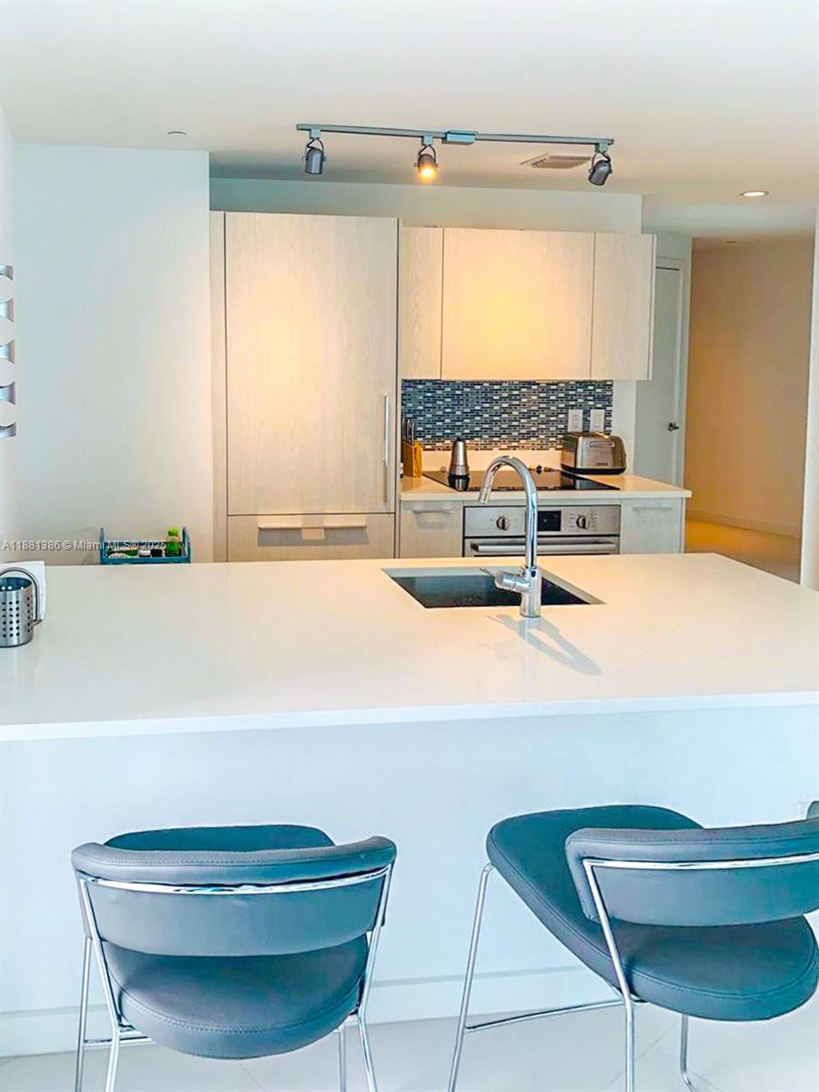 A modern kitchen features a white island, stainless steel appliances, and a blue tiled backsplash — 501 NE 31st St # 3906, Miami FL 33137, MIAMI, FL