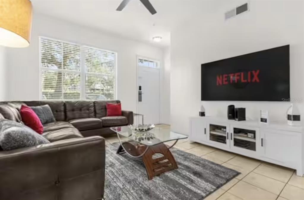 A living room features a dark leather sectional, glass coffee table, and wall-mounted television — 4015 VENETIAN BAY DRIVE UNIT 104, KISSIMMEE, FL
