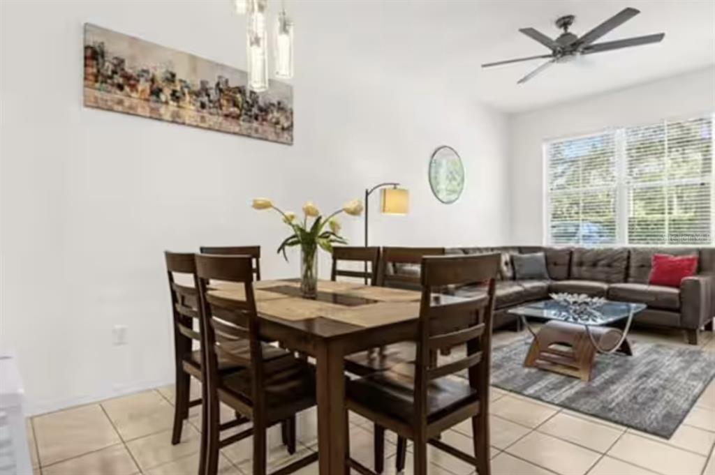 A dining area with a wooden table and chairs sits adjacent to a living room — 4015 VENETIAN BAY DRIVE UNIT 104, KISSIMMEE, FL