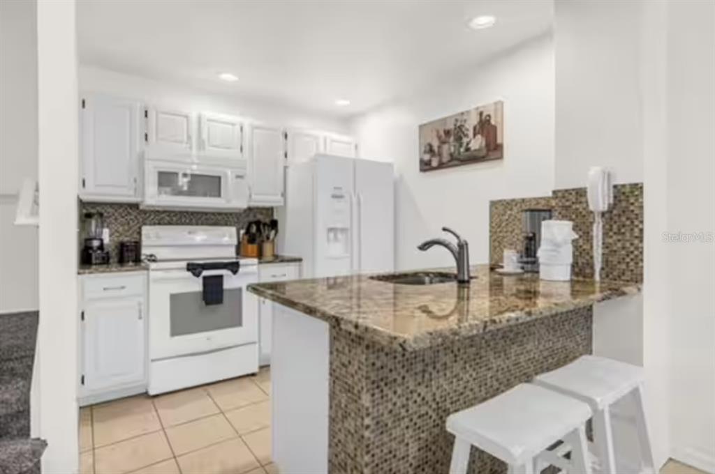 A kitchen features white cabinets, white appliances, a granite-topped island, and a tiled backsplash — 4015 VENETIAN BAY DRIVE UNIT 104, KISSIMMEE, FL