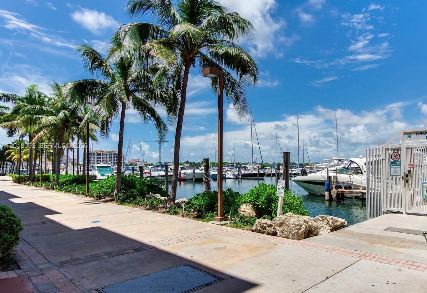 A paved walkway leads to a marina filled with boats under a sunny blue sky — 90 Alton Rd # 1804, Miami Beach FL 33139, MIAMI BEACH, FL