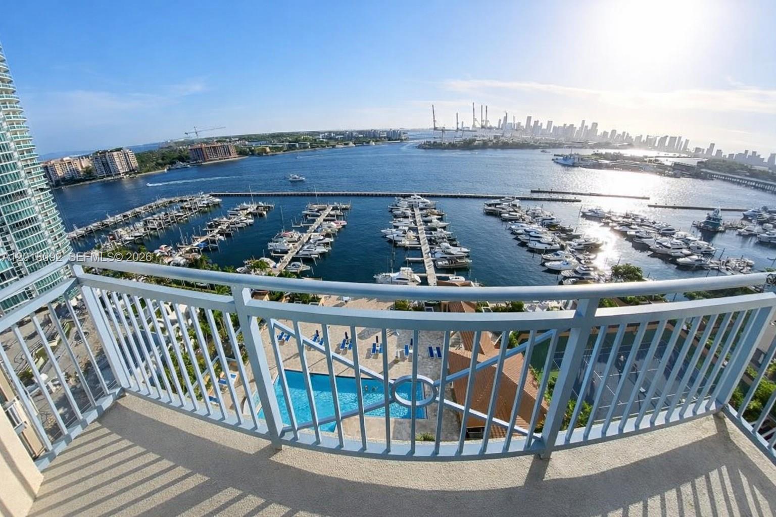 A high-angle view from a balcony overlooking a marina, swimming pool, and city skyline — 90 Alton Rd # 1804, Miami Beach FL 33139, MIAMI BEACH, FL