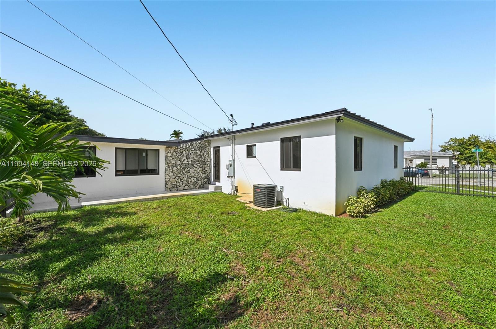 The exterior of a white house features a stone accent wall and a grassy backyard — 5152 SW 6th St, Miami FL 33134, MIAMI, FL