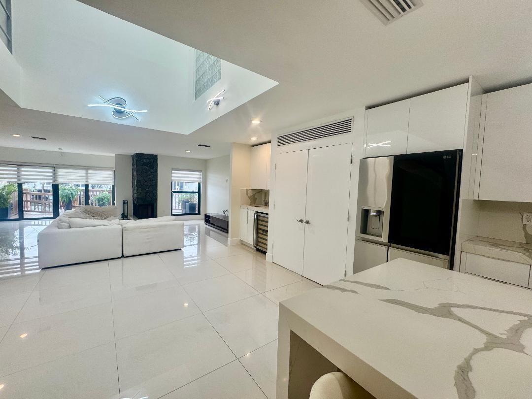 A modern open-concept kitchen and living area featuring white cabinetry, marble countertops, and tiled floors — 1127 Boca Cove Lane, Highland Beach FL 33487, HIGHLAND BEACH, FL