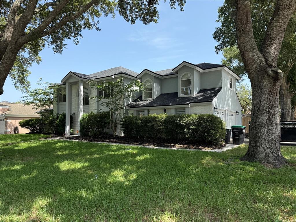 A two-story white brick house with a front walkway and mature trees in the yard — 1927 PALM VIEW DRIVE, APOPKA, FL